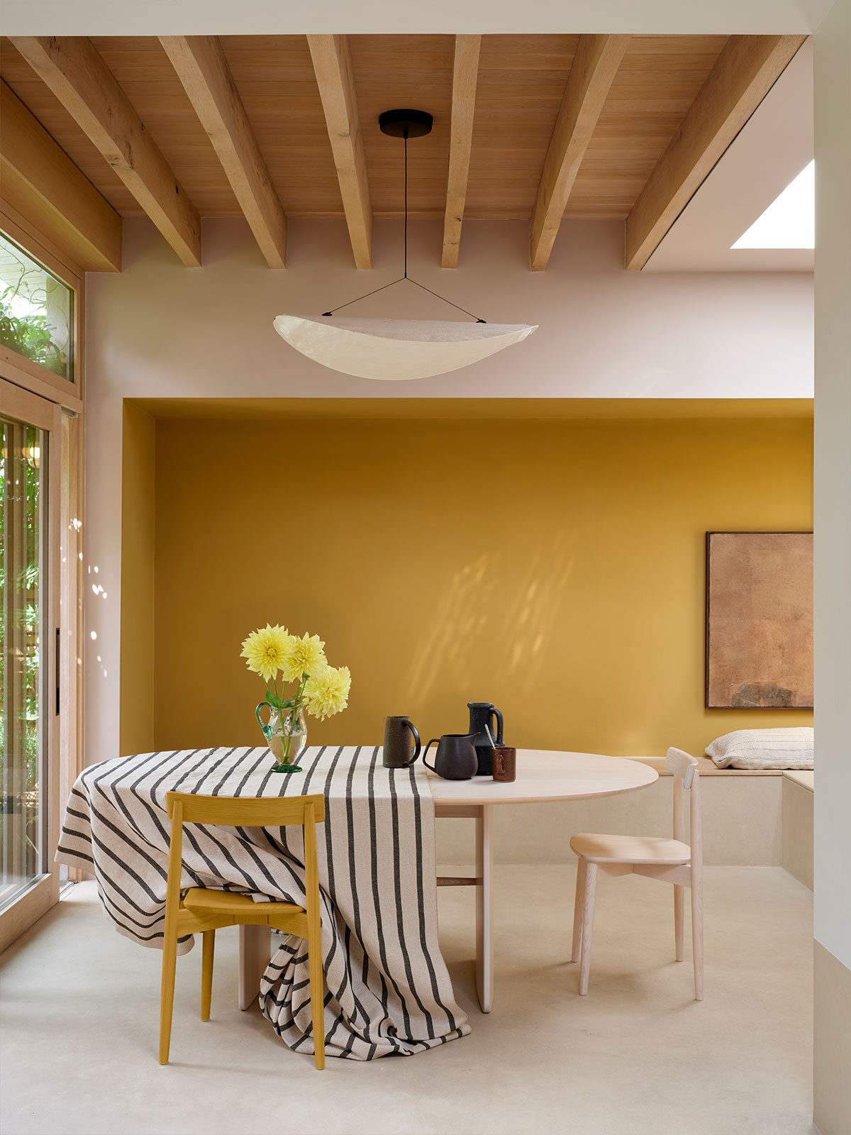 A modern dining area with a striped tablecloth, mixed chairs and yellow flowers on the table.