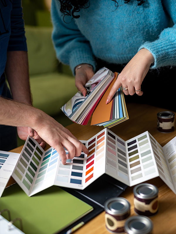 Two people looking at paint colour swatches and fans on a wooden table. 