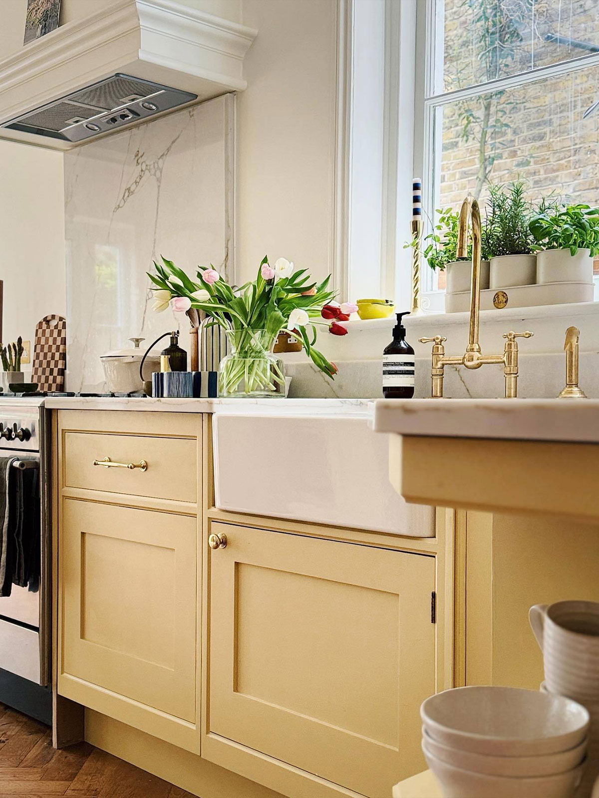 A bright kitchen with pale yellow cabinets, a farmhouse sink and a vase of tulips on the counter.