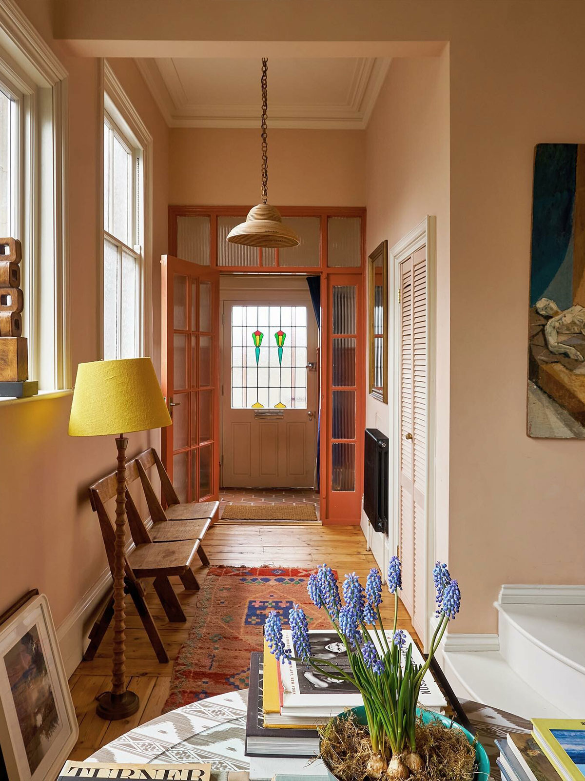 A warm hallway with peach walls, wooden chairs, a yellow lamp and a stained‑glass door.