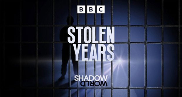 A dark BBC banner featuring the title “Stolen Years: Shadow World” in large white text. Behind the words, a silhouetted figure stands behind prison bars, lit by bright torchlight.