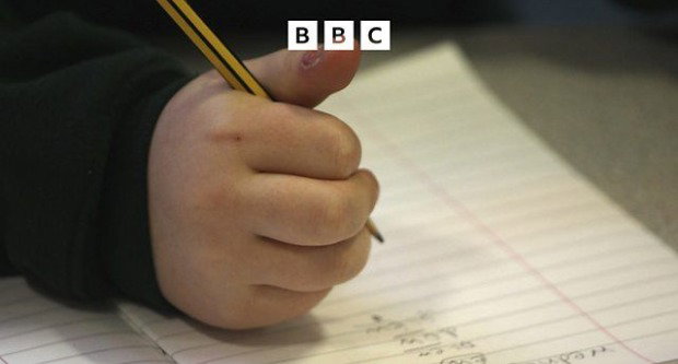 The hand of a child holds a yellow and black pencil over lined paper with written notes.