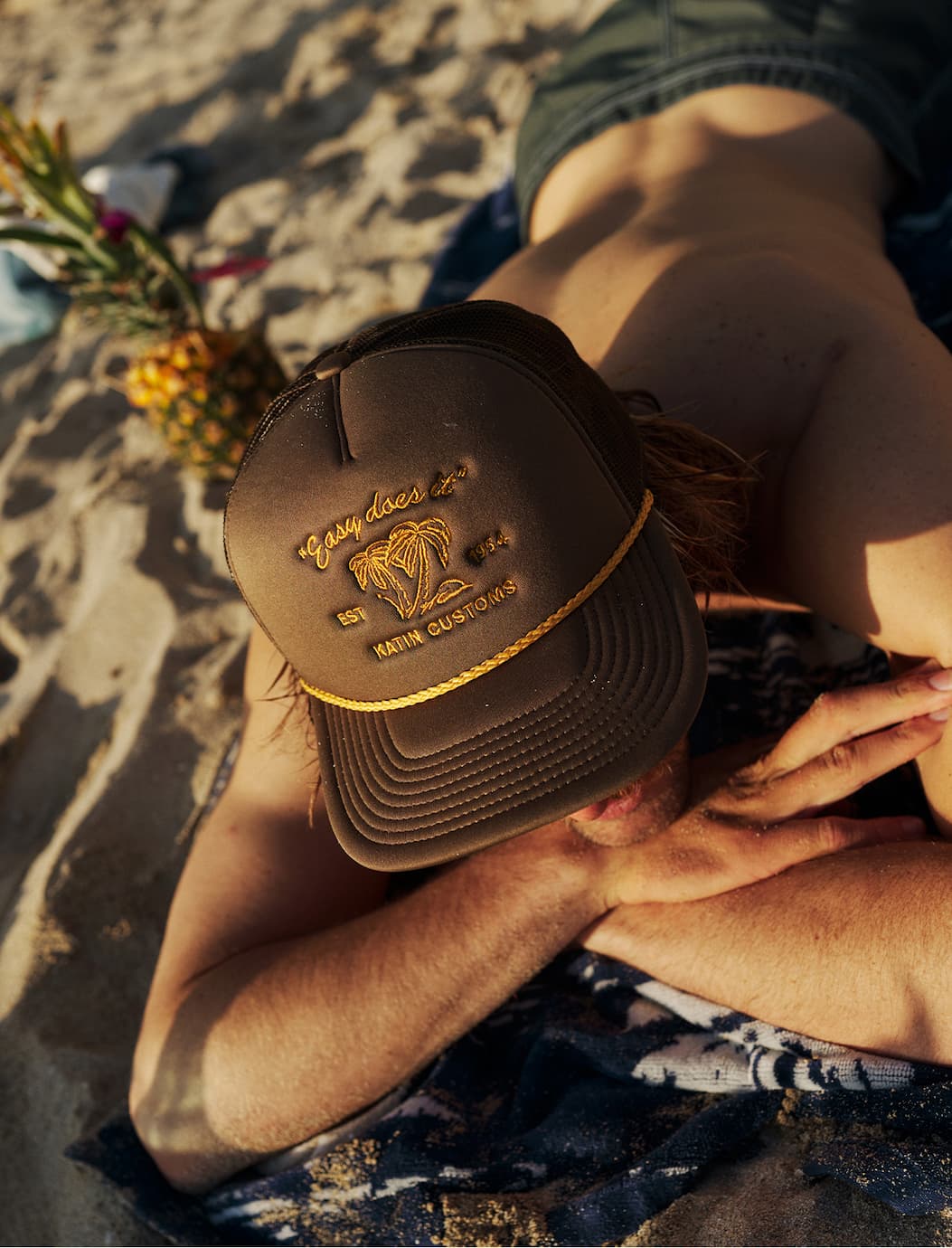Model laying out on beach wearing the Suds Trucker Hat