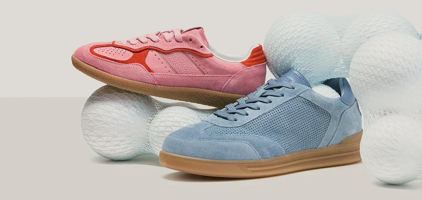 Rosa und blaue Wildlederschuhe mit Gummisohlen, platziert zwischen großen weißen, strukturierten Kugeln auf einem neutralen Hintergrund.