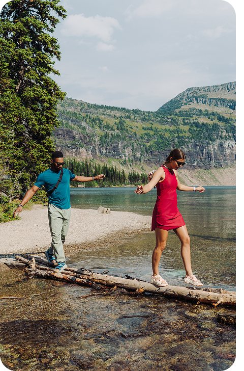 An image of two people balancing while walking on a tree branch to cross the stream.