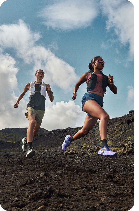 An image of two people running on a dirt path along a mountain slope. 