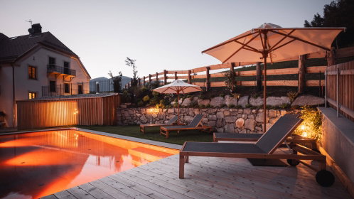 Hotel Außenansicht mit Pool, einer Liege und Sonnenschirm abends