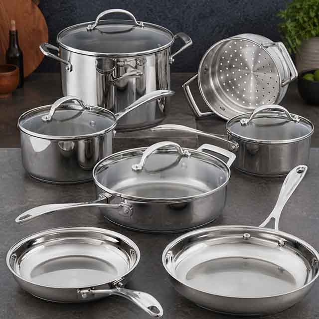 A set of shiny stainless steel cookware on a kitchen surface, including a large pot with a lid, several saucepans with lids, a sauté pan, a steamer basket, and two frying pans. A bottle and wooden utensils are in the background.