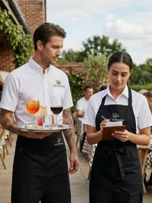 Due camerieri in camicia bianca e grembiule nero servono i clienti nel giardino di un ristorante