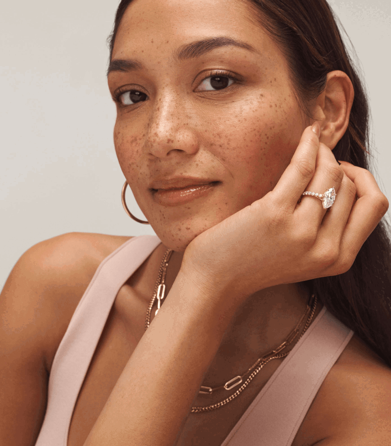 Woman wearing yellow gold hoop earrings, layered chains, and a marquise-shaped diamond ring on pavé band.