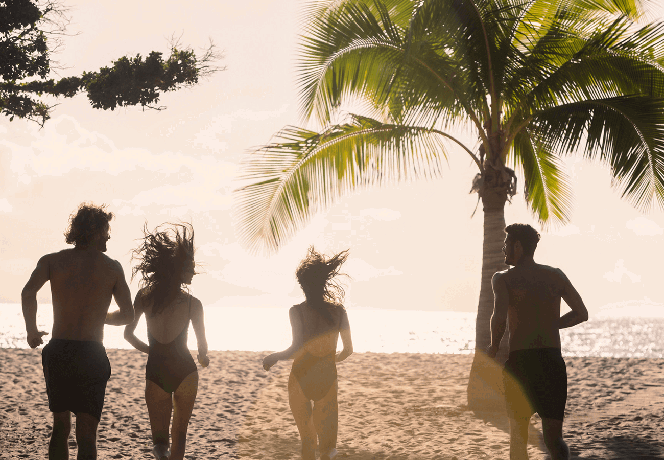 Four guests run toward a sandy beach and the ocean.