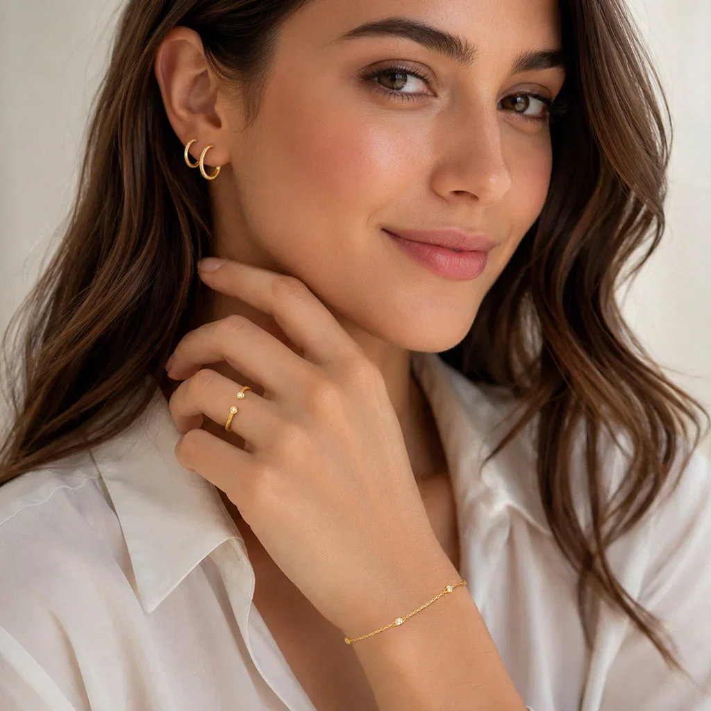 Woman wearing gold jewelry from Outlet Selects collection including hoop earrings, ring, and delicate bracelet against neutral background.