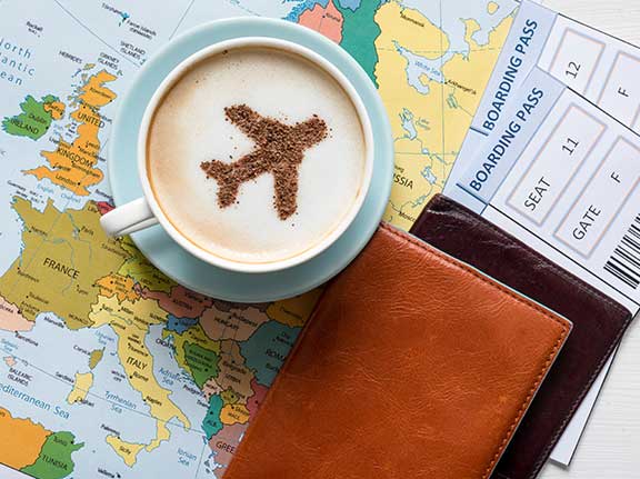 Tasse mit Milschaum und Flieger aus Kakaopulver steht auf Landkarte. Daneben liegt ein Boardingpass.