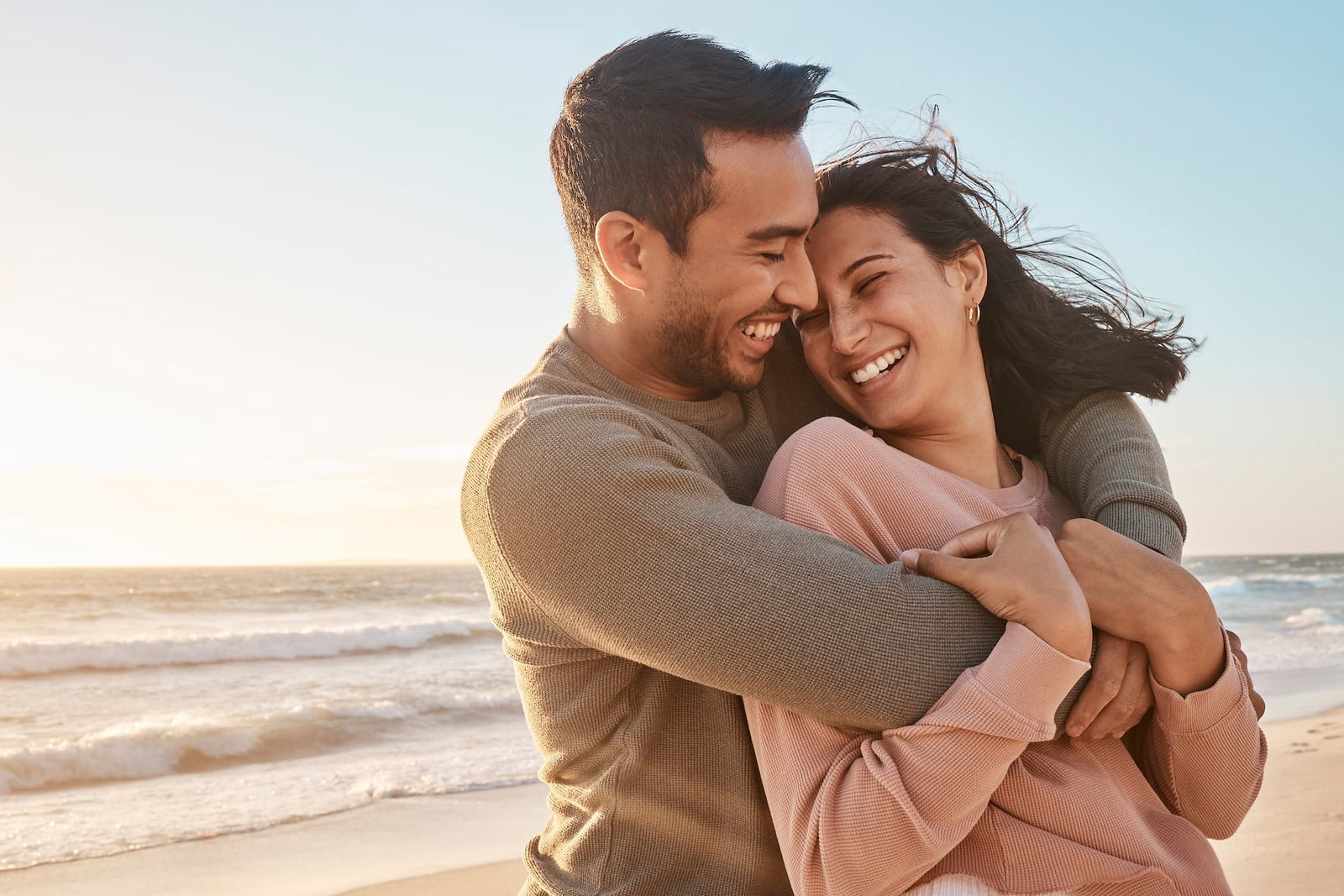 Couple smiling on the beach with man hugging the woman from behind