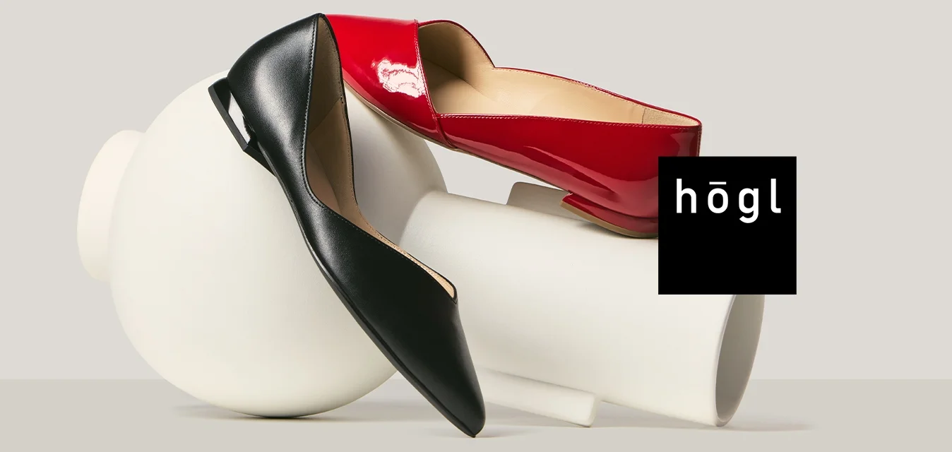 Zwei High-Heels, einer rot und einer schwarz, liegen auf und um weiße, zylindrische und kugelförmige abstrakte Formen.