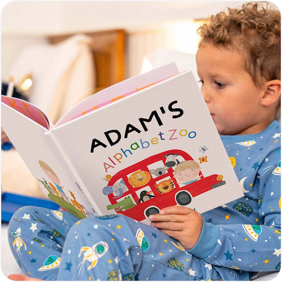 A young child in pyjamas reading a personalised book titled "Adam's Adventure"