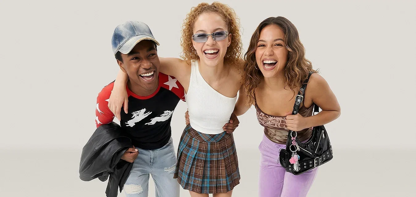 Trois jeunes femmes souriantes marchant en avant, habillées de tenues décontractées et colorées sur un fond clair uni.