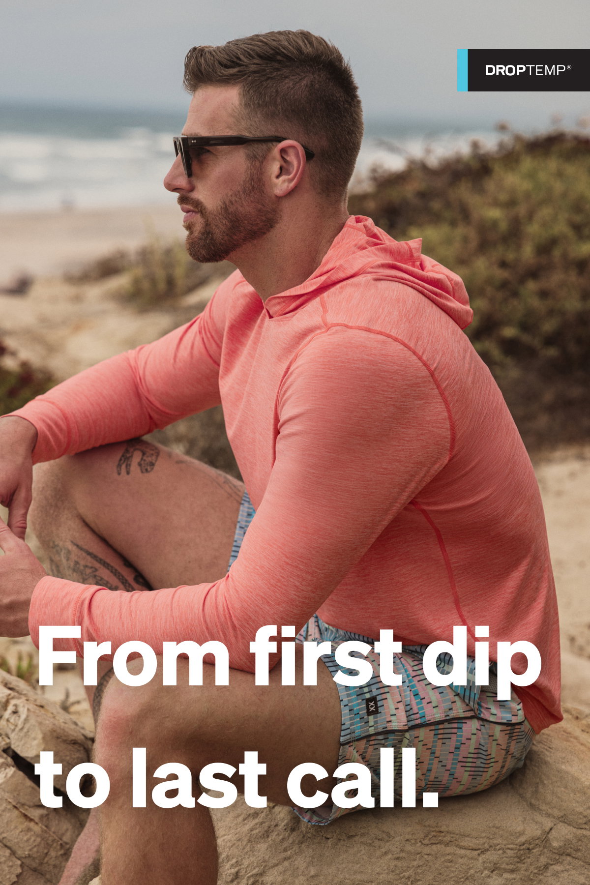 Man wearing a coral SAXX performance hoodie sitting on a beach, with “From first dip to last call” text overlay.
