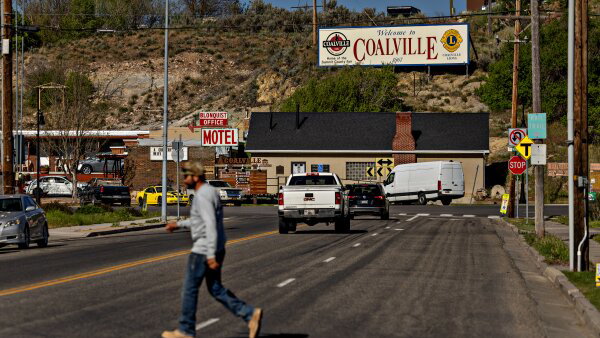 A man walks across a street that is in front of a Welcome to Coalville sign. 