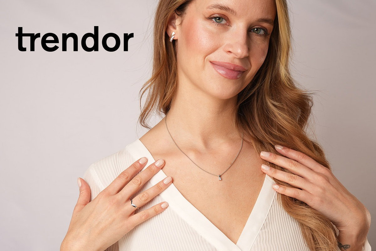 Eine Grafik von trendor Schmuck. Auf dem Foto ist der Kopf einer Dame zu sehen, die Schmuckstücke von trendor, eine Halskette, Ohrringe und einen Ring, präsentiert. 