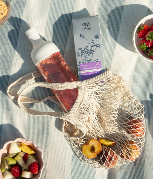 A drawstring bag on picnic mat with cold brew tea bottle and peaches