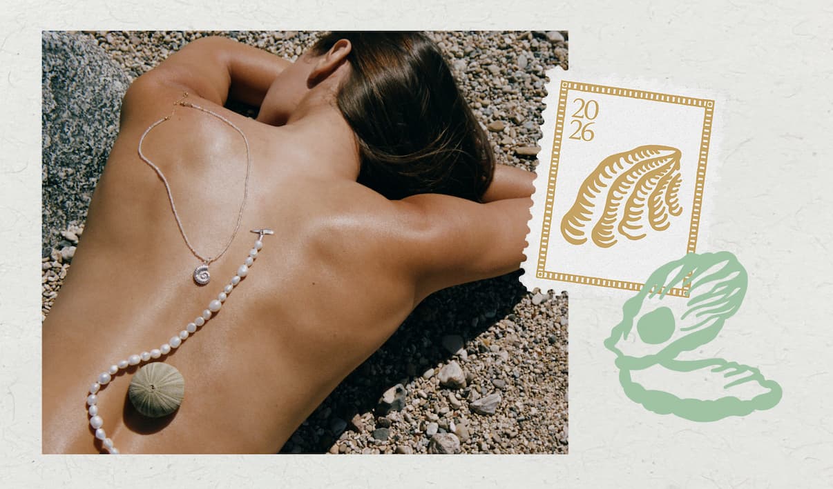 Model lying on a pebble beach wearing a pearl beaded necklace with spiral shell pendant and a delicate chain necklace.