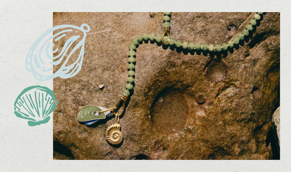 Green aventurine beaded necklace with gold ammonite charm and carved stone charm, laid on textured rock surface.