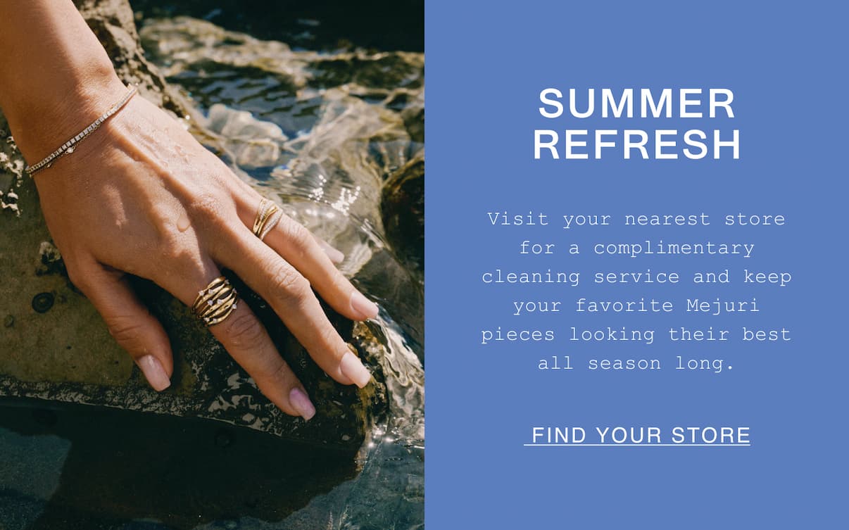 A close-up of a hand resting on a wet rock, wearing a gold multi-band ring, a gold ridged statement ring, and a delicate diamond tennis bracelet. Beside the image, text on a periwinkle blue background reads "Summer Refresh — Visit your nearest store for a complimentary cleaning service and keep your favorite Mejuri pieces looking their best all season long." with a "Find Your Store" call-to-action link.