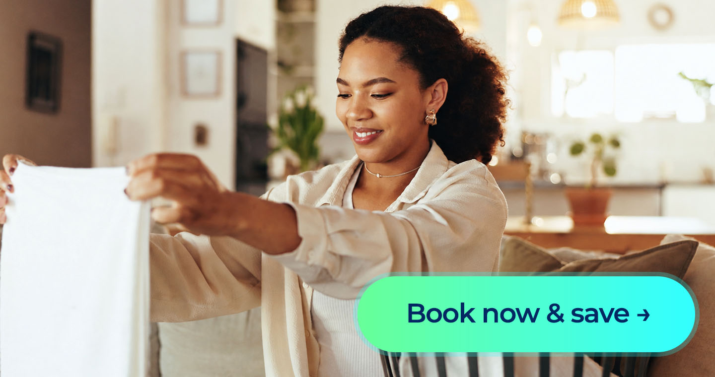 Smiling woman folds laundry beside a basket with a “Book now & save” button displayed.