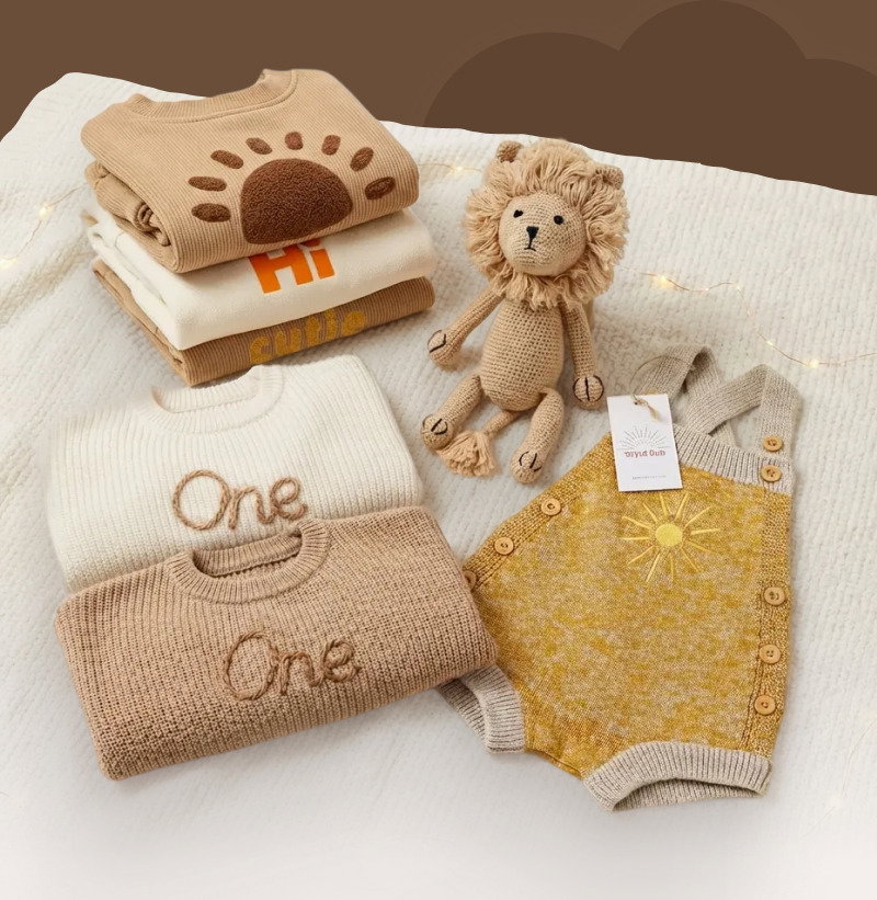 Flat lay of soft baby gifts including a personalized blanket, plush toys, knit items, and neutral nursery accessories.