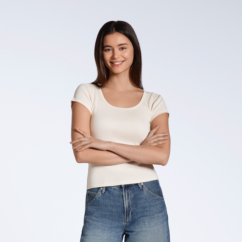 A woman smiling with her arms crossed, modelling a natural coloured, organic cotton scoop neck t-shirt.