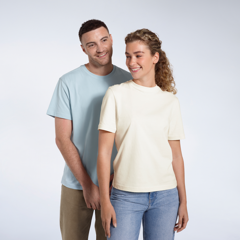 A man and woman smiling, modelling short sleeve, light blue and ecru coloured organic cotton t-shirts.