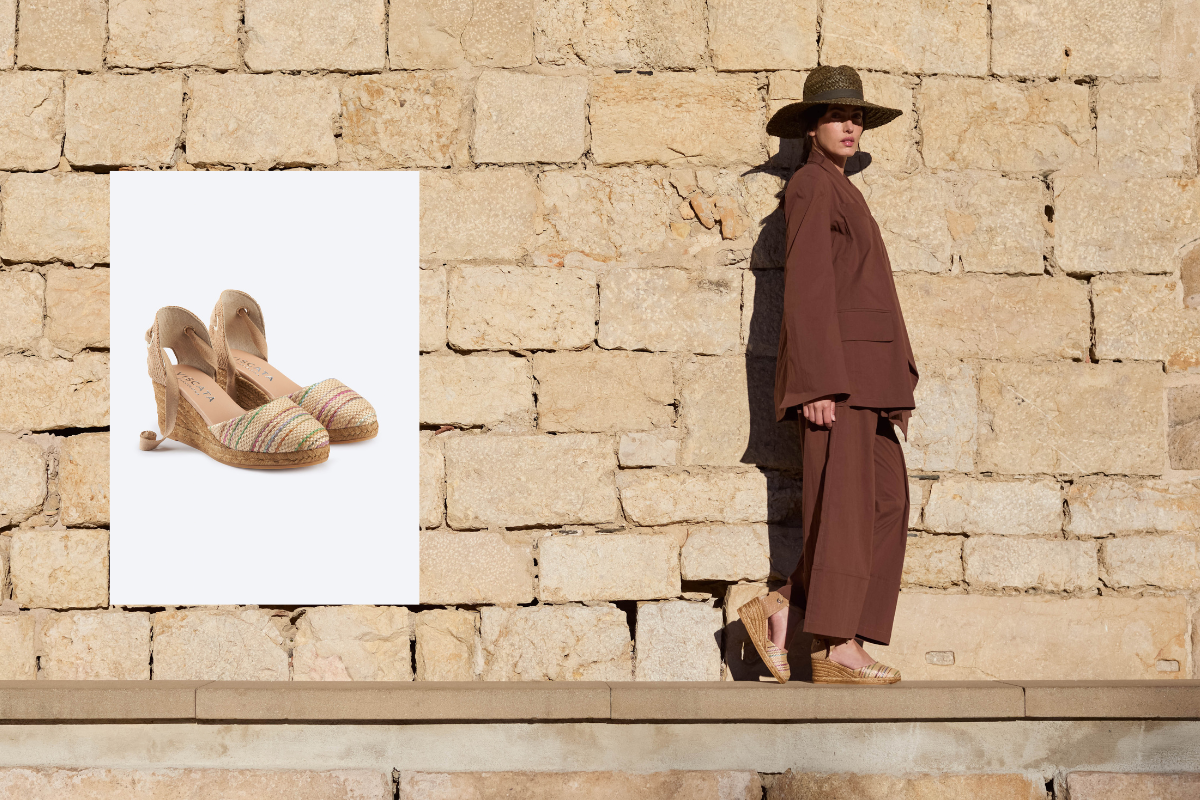 Striped espadrille slingback flats styled with a relaxed brown linen set against a Mediterranean stone wall.