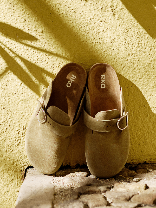 Pair of beige suede clogs with buckles on a textured yellow surface
