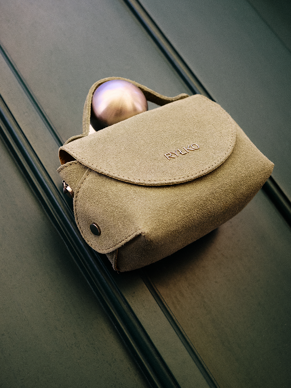Beige suede handbag with a metallic object on a textured surface