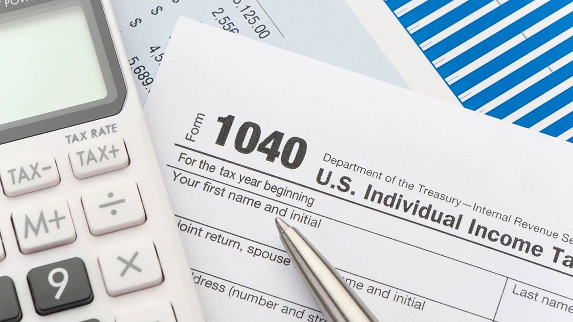 part of calculator with 1040 tax form and silver pen laying on it