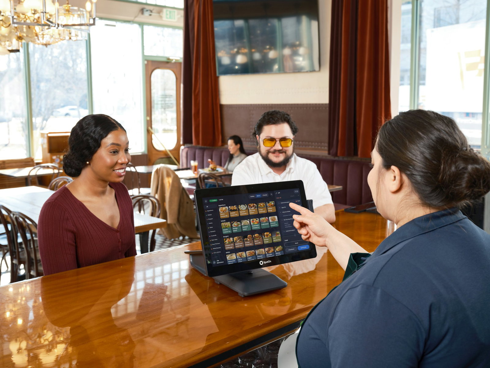 Server shows digital menu to customers at a bar.