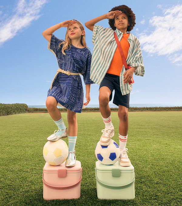 Two kids in stylish outfits, with footballs under their feet, stood on podiums. 