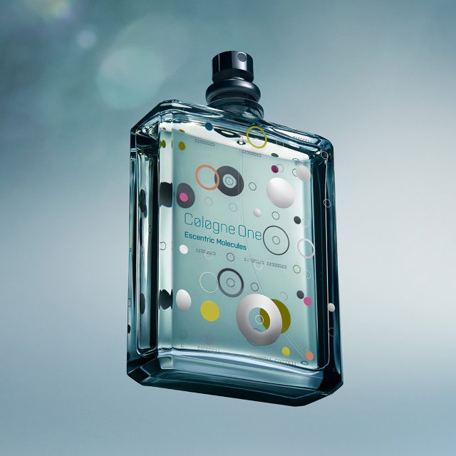 A stylish glass bottle of Escentric Molecules' Cologne One is suspended against a soft, blurred background. The bottle features a modern design with colourful circular patterns and the brand name, creating a sleek and contemporary appearance.