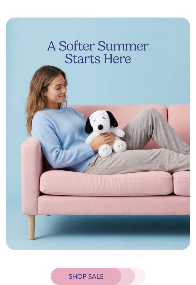 A woman relaxing on a couch with Snoopy Warmies. Shop Sale.
