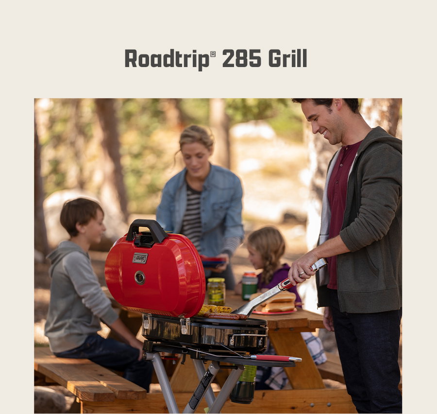 Text reads Roadtrip 285 Grill. People gather around a picnic table near a portable red grill outdoors.