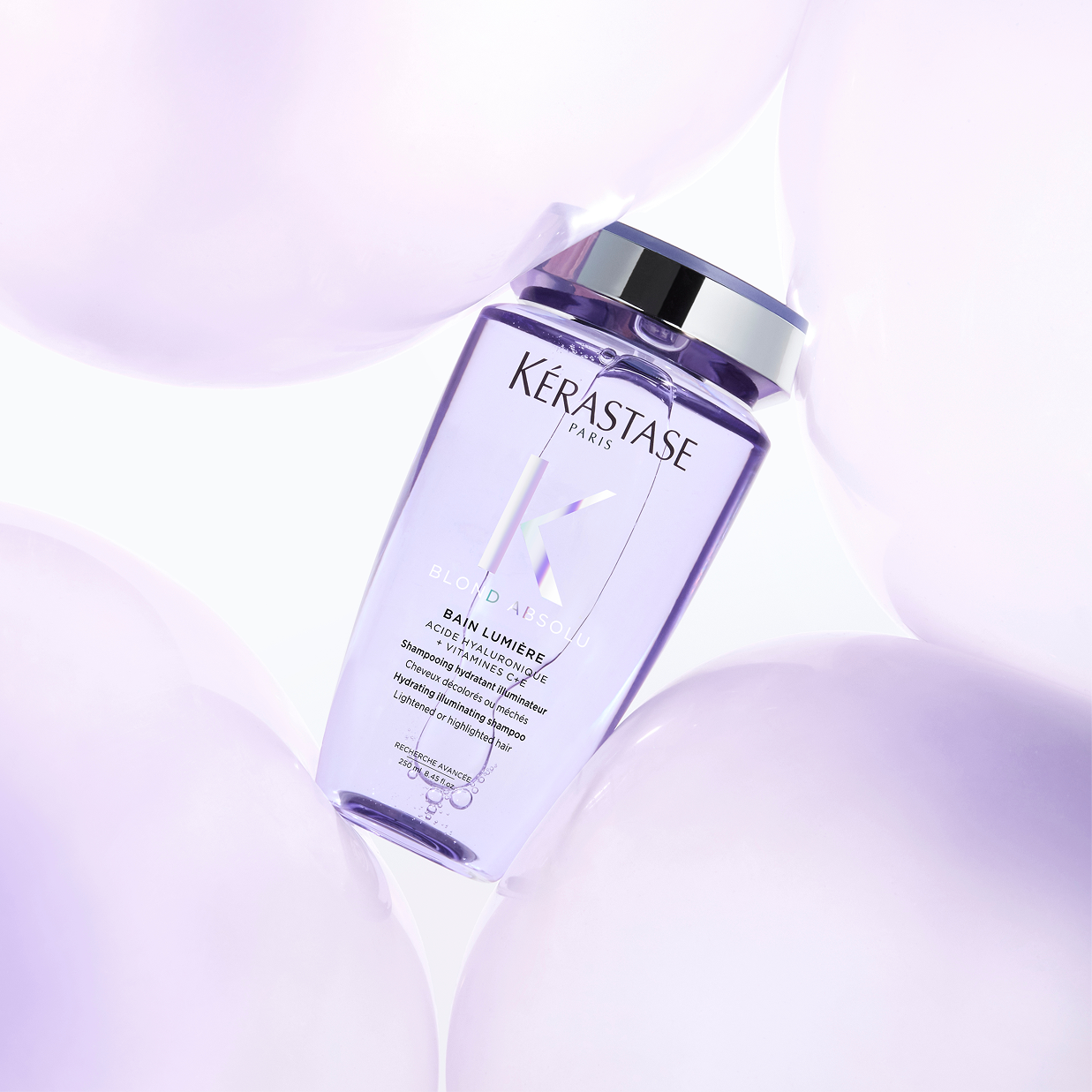 Flacone di shampoo Kérastase Blond Absolu Bain Lumière viola trasparente circondato da sfere lilla
