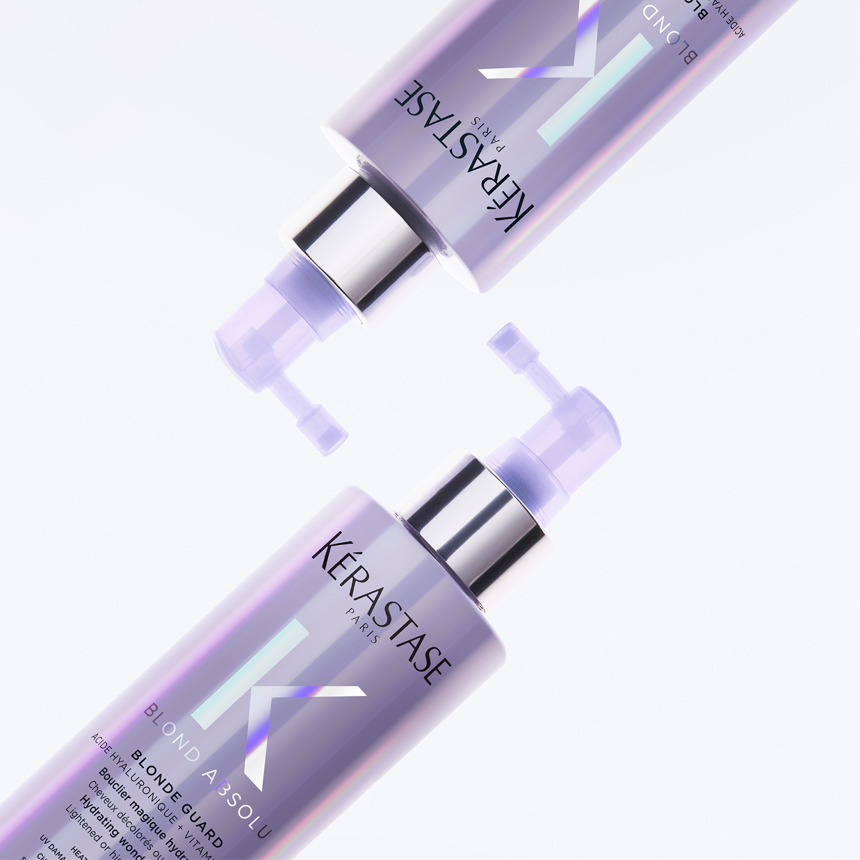 Due flaconi spray di Kérastase Blond Absolu Blonde Guard disposti in diagonale su sfondo bianco e lilla