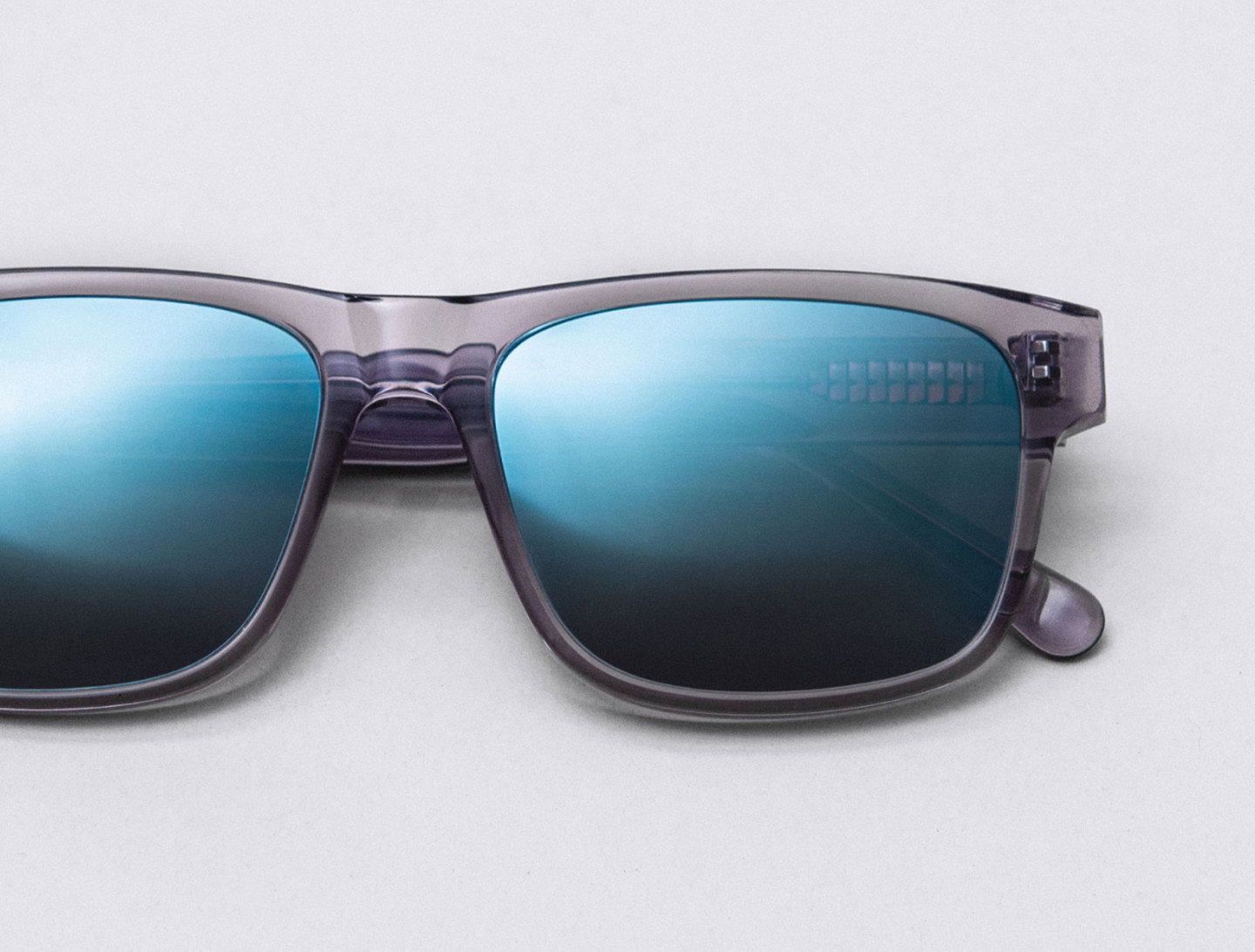Nahaufnahme einer Sonnenbrille mit grau/transparentem Rahmen und blau verspiegelten Gläsern