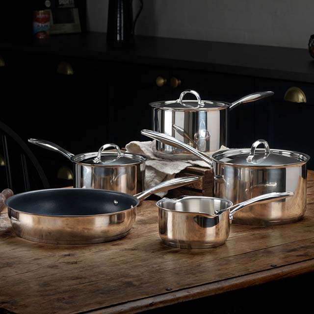 A set of shiny Stellar stainless steel cookware with lids on a wooden table.