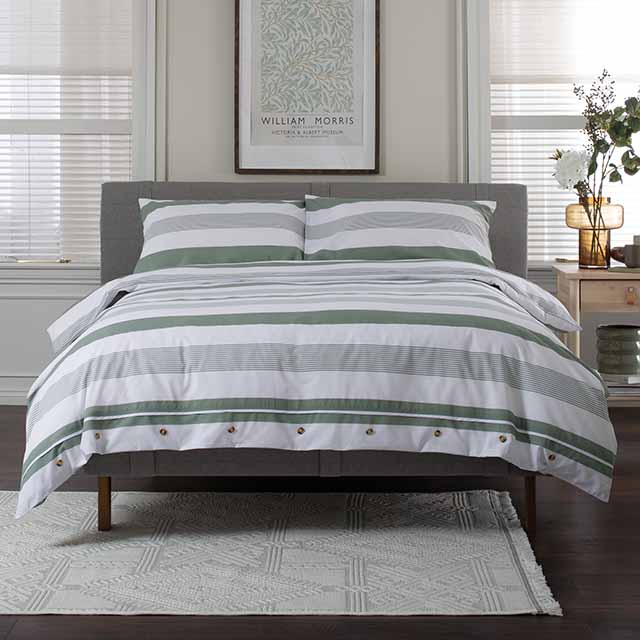 A bed with striped bedding is positioned beneath a framed artwork, flanked by nightstands with lamps and plants, in a well-lit room.