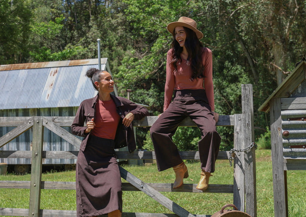women in chocolate brown corduroy sitting on a fence in the country 