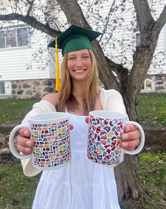 Graduate holding two art mugs