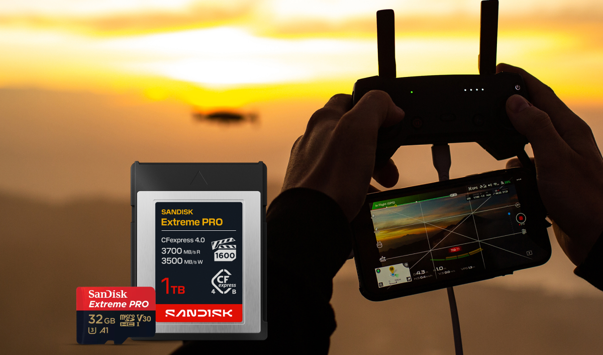 A SANDISK Extreme PRO CFexpress and a SanDisk Extreme PRO microSD card displayed alongside a person holding a drone remote control and smartphone displaying drone footage with a sunset background.