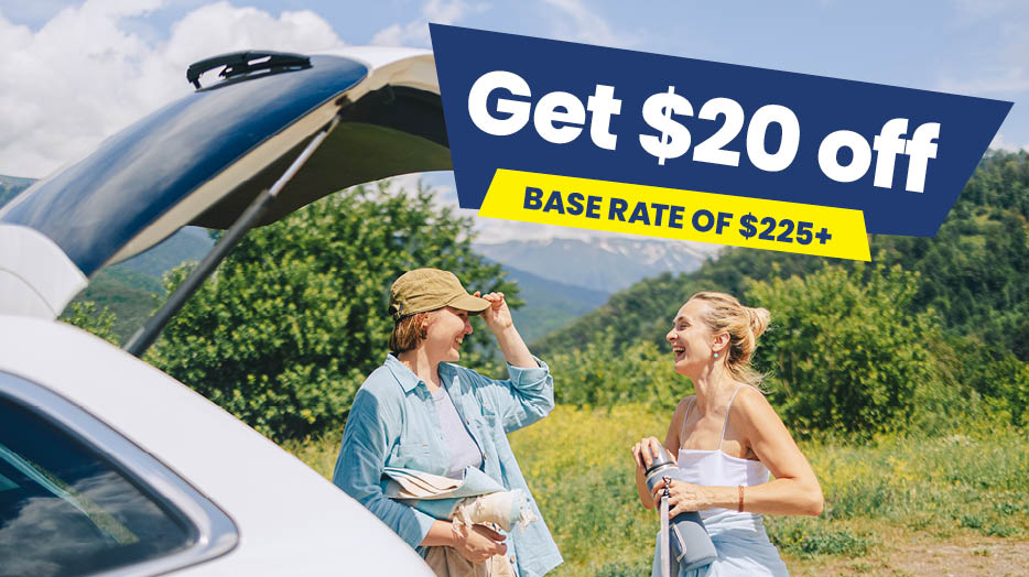 Get $20 off base rate of $225+. Two women standing beside an open vehicle trunk in a scenic outdoor setting. 